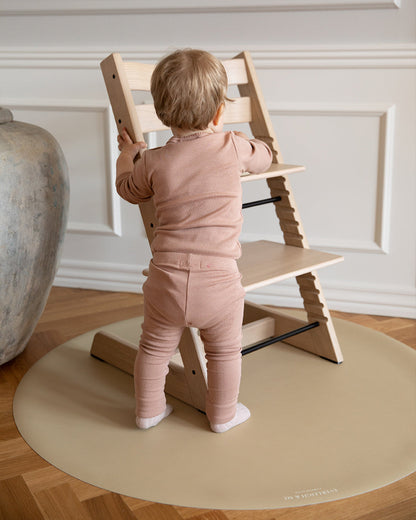  Et stoleunderlag fra Everleigh and Me ligger under en stokke højstol og beskytter gulvet. Et barn er ved at sætte sig på højstolen for at være klar til spisestid. stoleunderlag ikea, silikone underlag, bord underlag, stol til baby, babystole