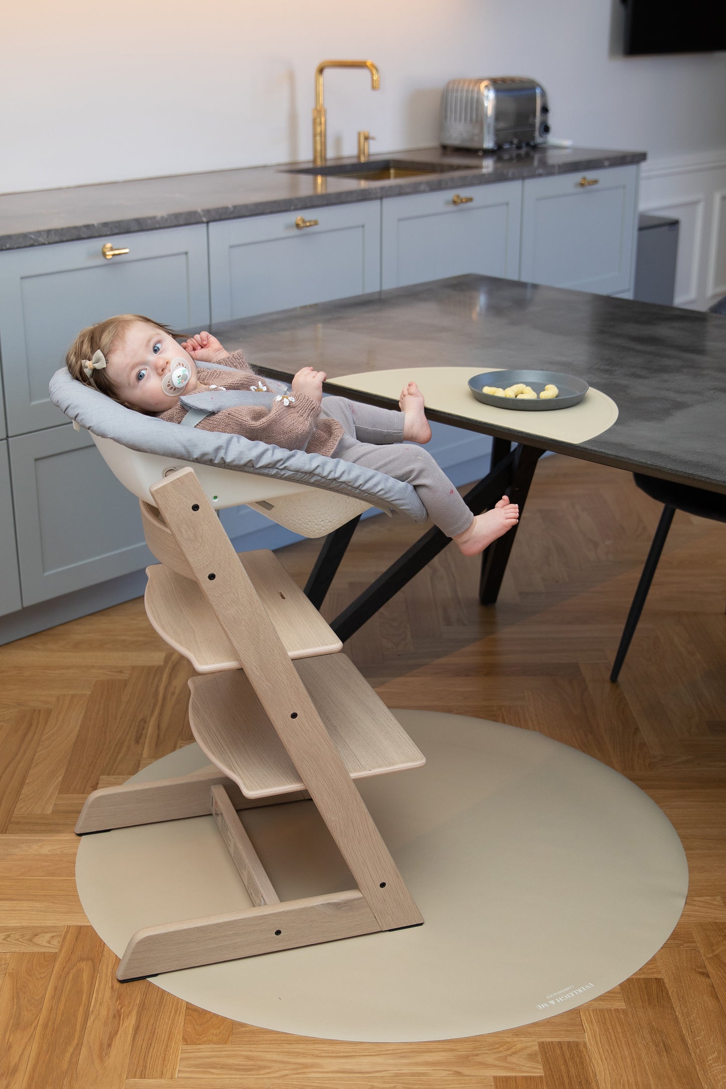 En baby sidder på en stokke træ højstol og spiser efter baby-led weaning-metoden, mens et stoleunderlag i farven Clay fra danske børnemærke Everleigh & Me beskytter gulvet mod spild. Underlaget smukt matcher gulvets farvetone. underlag gulv, baby stole, underlag kontorstol, plastmåtte