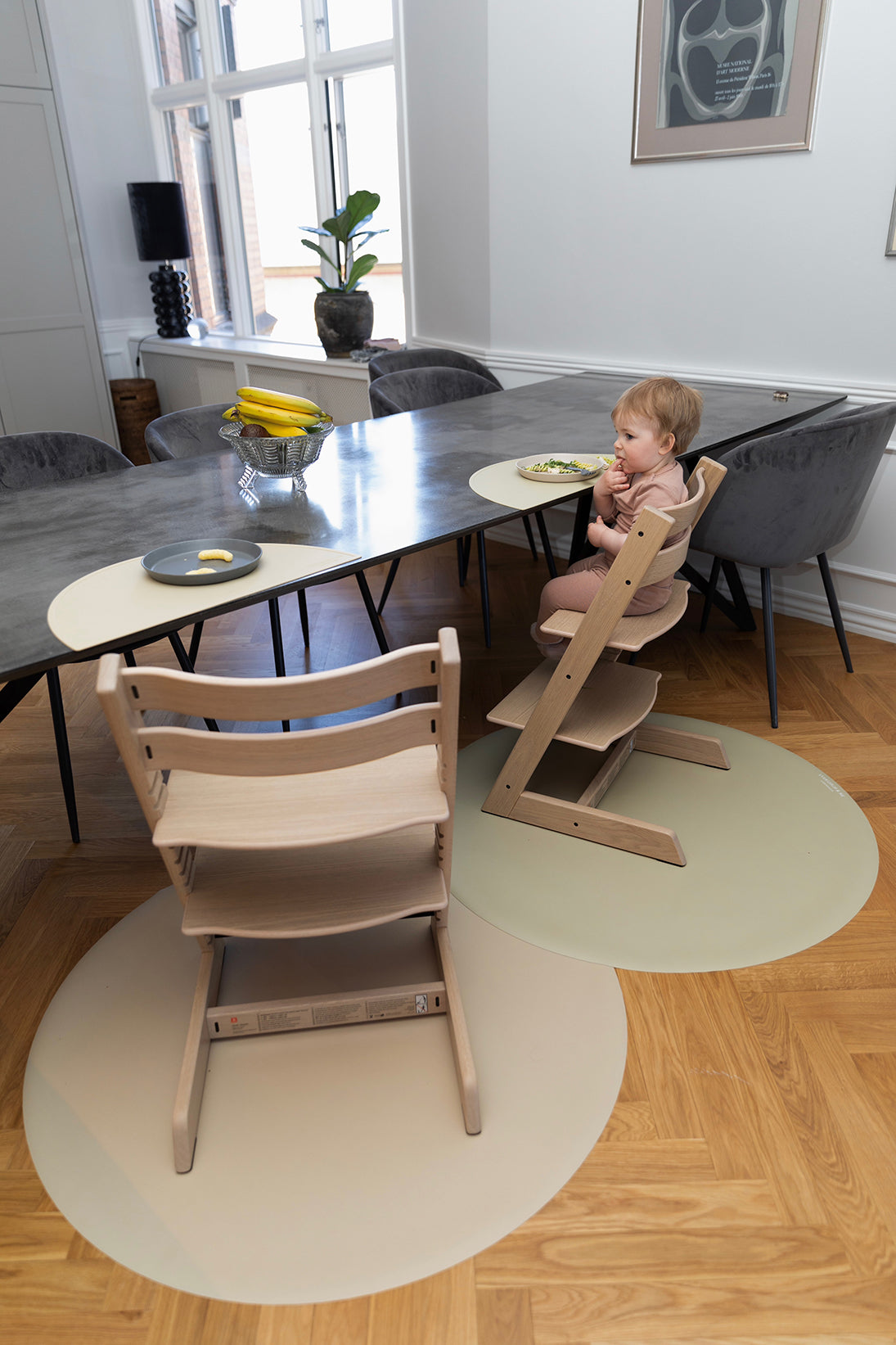 To små børn sidder og spiser på Stokke højstole, mens slidstærke stoleunderlag fra Everleigh and Me i farven Clay beskytter gulvet mod madrester. Underlagene tilføjer både praktisk beskyttelse og et stilfuldt touch til det designinspirerede hjem, stoleunderlag baby, måtte under højstol, underlag til højstol, everleigh and me underlag