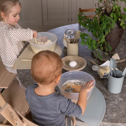 To børn sidder og laver mad på højstole med hver deres skål. De bruger silikone køkkenredskaber fra Everleigh and Me til at bage muffins. Køkkenredskaber passer perfekt til de små barnehænder og inviterer børnene til aktivt at deltage i bagningen.